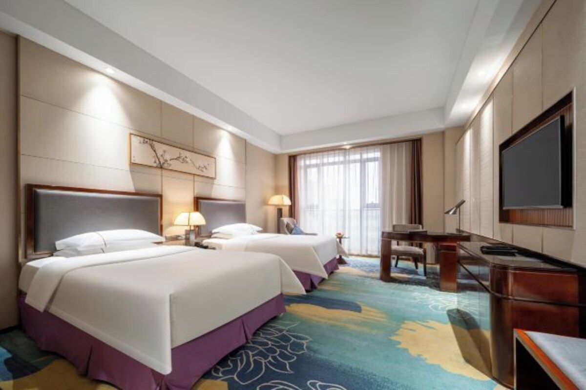 Une chambre d’hôtel avec deux lits, un bureau, une télévision et une grande fenêtre avec des rideaux.