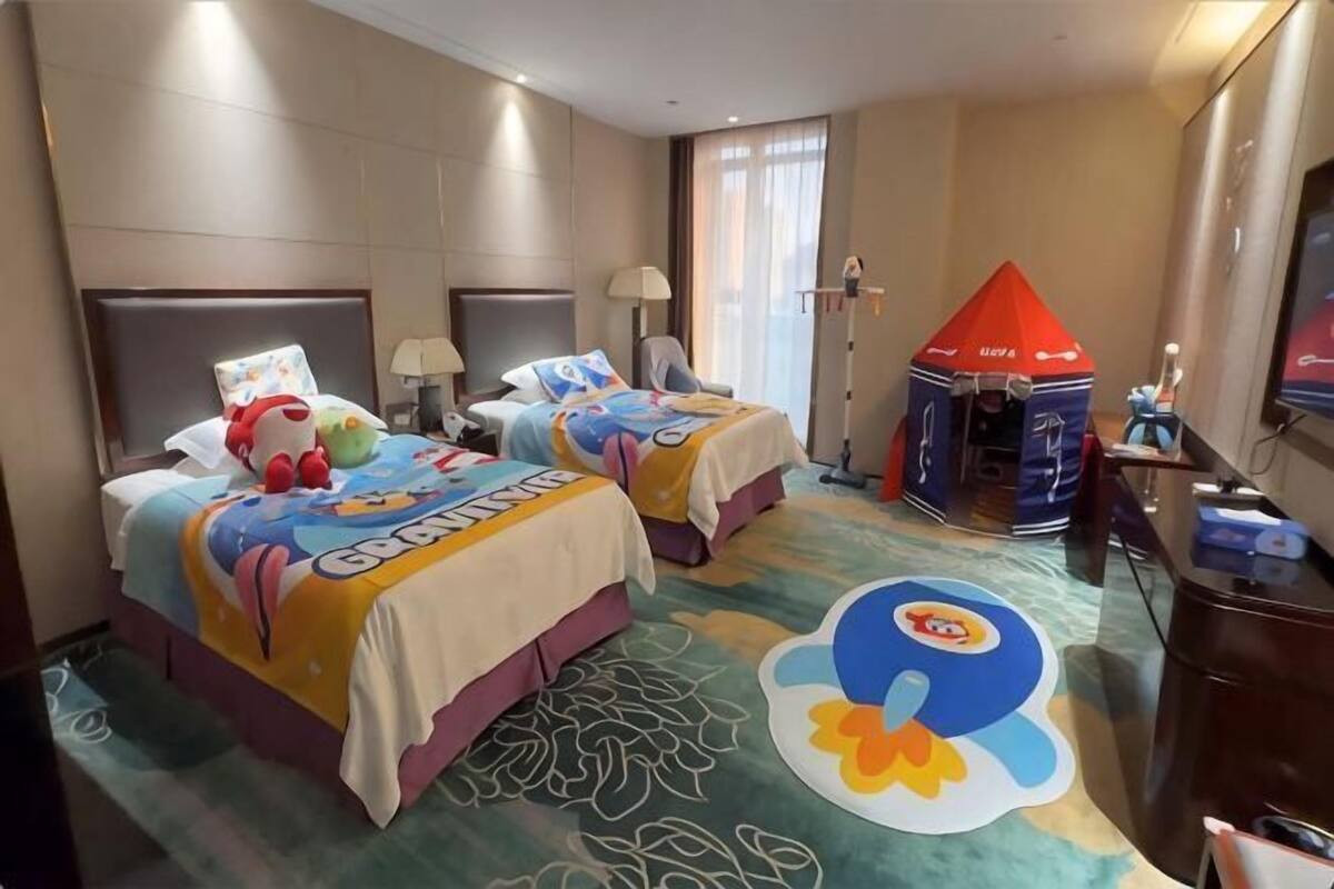 Ein Hotelzimmer mit zwei Betten, einem Spielzelt und einer großen Zeichentrickfigur auf dem Teppich.