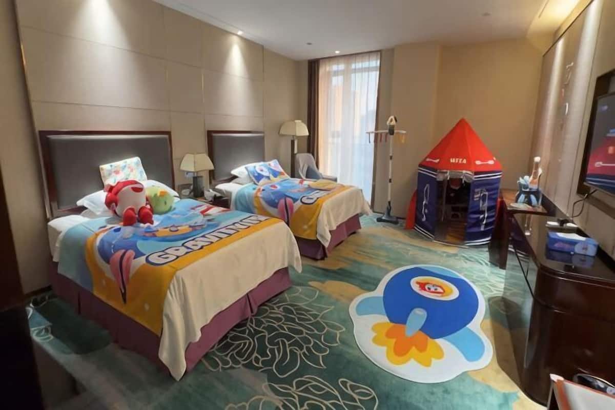 Une chambre d’hôtel avec deux lits, une tente de jeu et un grand motif représentant un personnage de dessin animé sur le tapis.