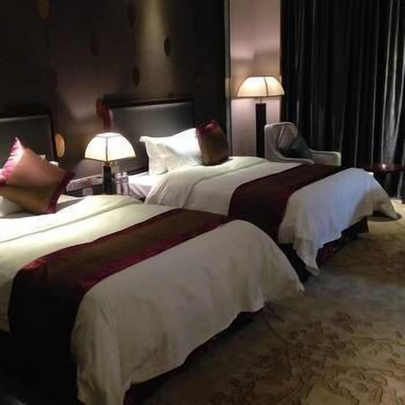 A hotel room with two beds, a nightstand, lamps, and a chair.