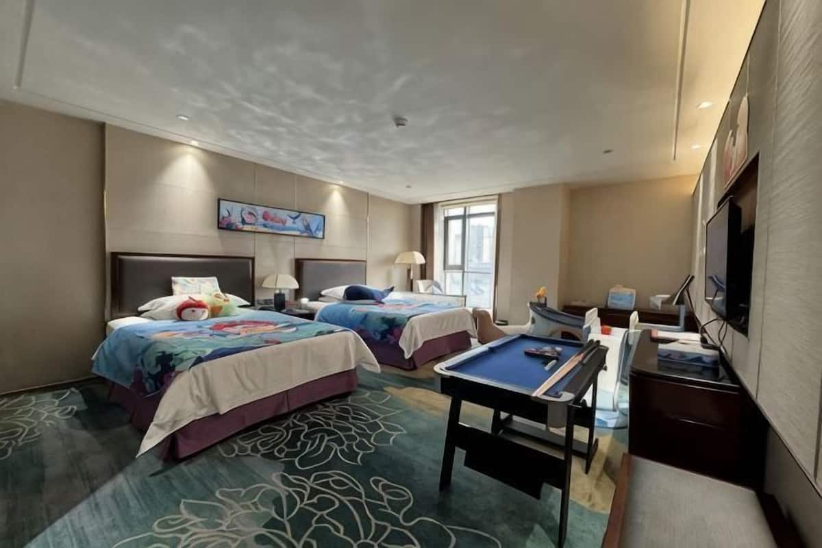 Une chambre d’hôtel avec deux lits, une table de billard, un téléviseur et une grande fenêtre.
