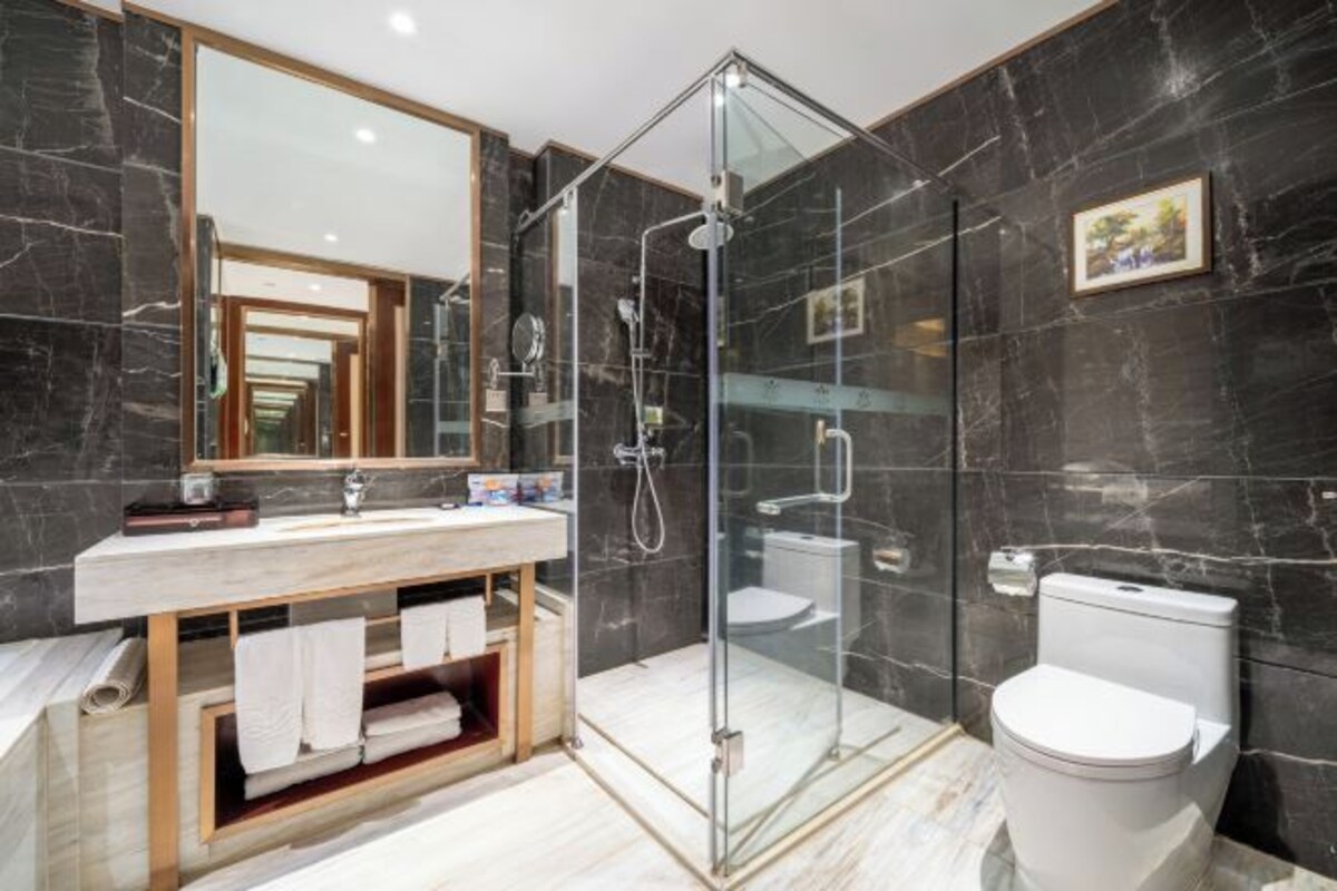 Une salle de bain moderne avec une douche à parois de verre, un mur recouvert de carreaux de marbre, un meuble-lavabo en bois et des toilettes blanches.