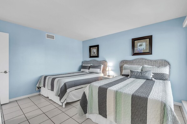 A bedroom with two beds, a door, and a framed picture on the wall.