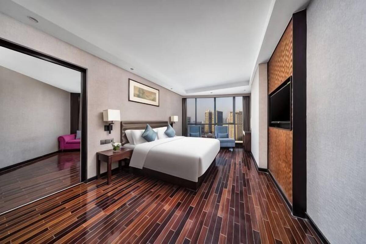 A hotel room with a large bed, a TV, a city view, and a wooden floor.