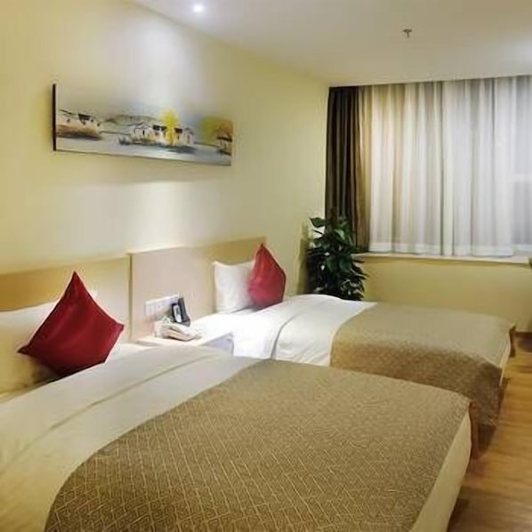 A hotel room with two beds, a painting on the wall, a window with curtains, and a plant.