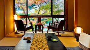 A traditional Japanese room with tatami flooring, a low table with a tea set, and two rocking chairs facing a large window with a view of autumn trees and a house. - Heihachi Tea House Inn (Kyoto)