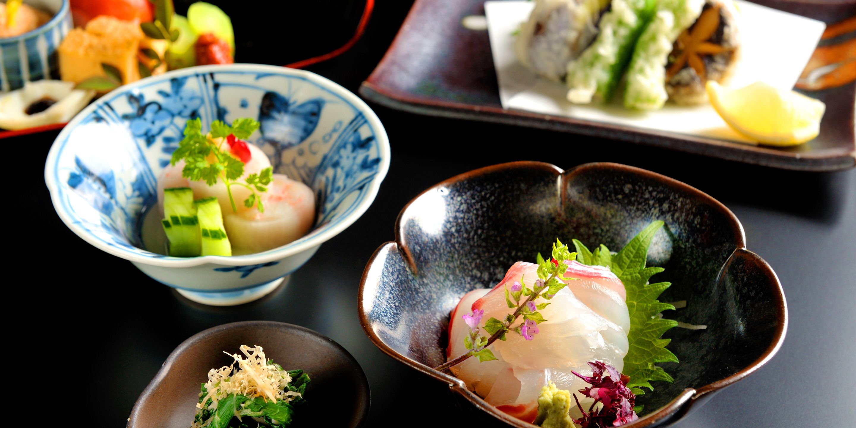 A variety of dishes, including sashimi and sushi, served in traditional Japanese bowls.