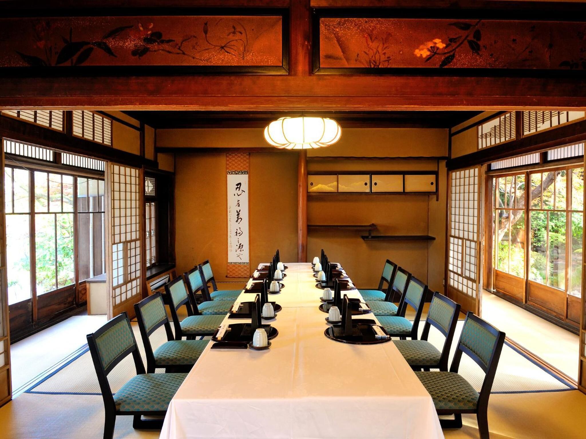 Ein traditioneller japanischer Raum mit Tatami-Matten, einem langen Tisch, der für eine Mahlzeit gedeckt ist, und verschiebbaren Türen.