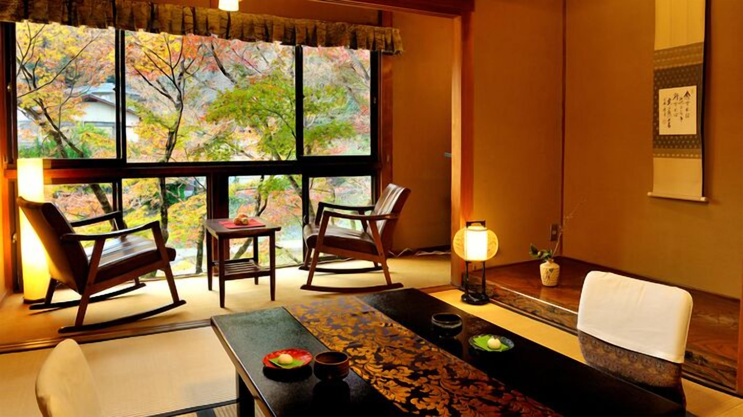 A traditional Japanese room with tatami flooring, a low table with a decorative runner, two rocking chairs, a small table with a candle, and a view of autumn trees through large windows.