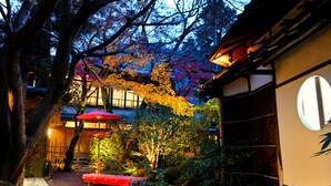 A traditional Japanese garden with a wooden bench, a red umbrella, and a building with a circular window. - Heihachi Tea House Inn (Kyoto)