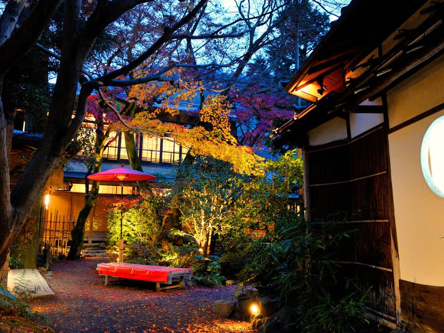 A traditional Japanese garden with a wooden bench, a red umbrella, and a building with a circular window.