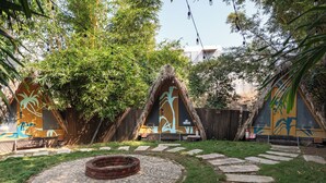 Un espace jardin comprenant un foyer circulaire en pierre, une clôture en bois et une structure à toit de chaume.