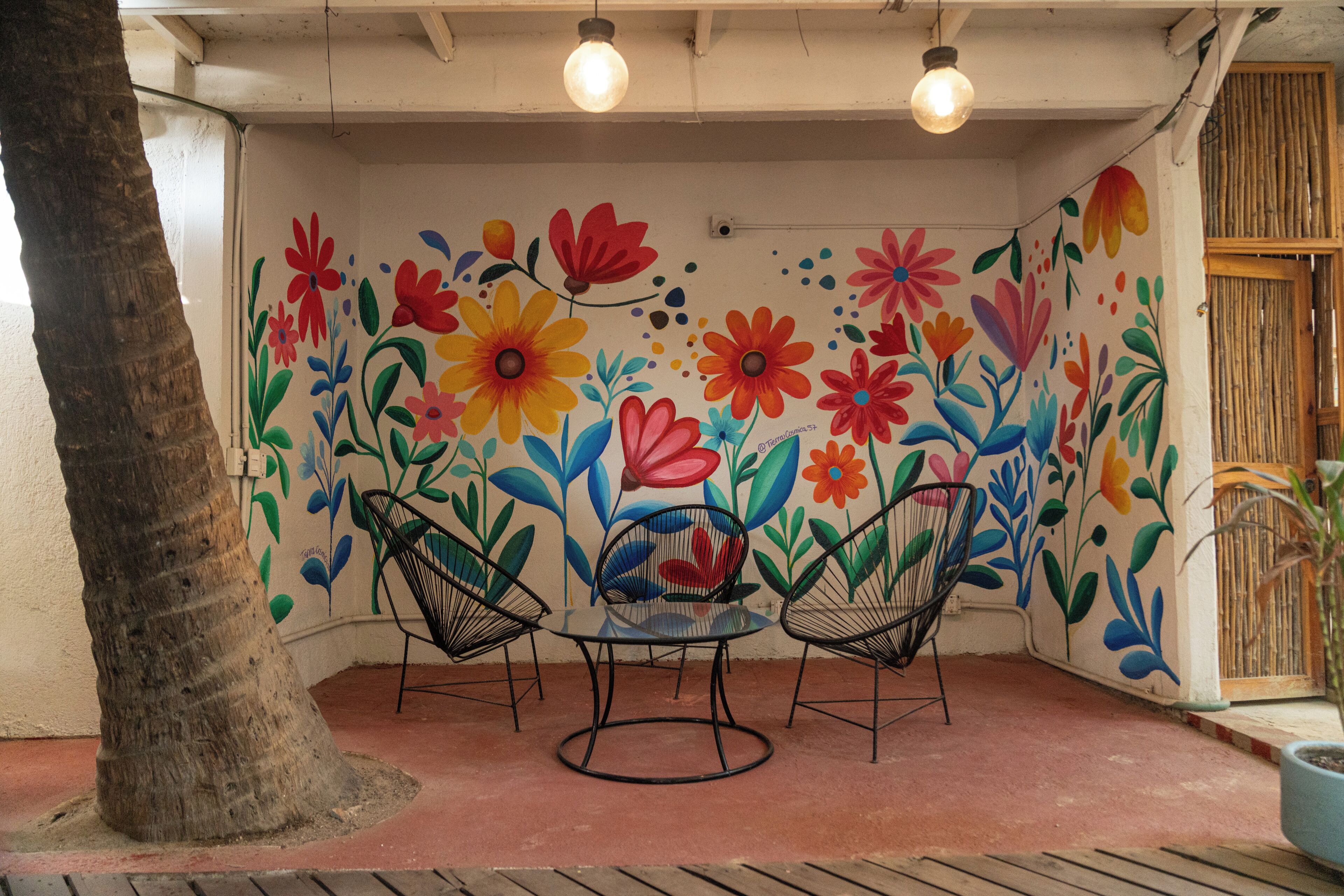 Une terrasse agrémentée d’une fresque représentant des fleurs aux couleurs vives, de deux chaises en métal et d’une table.