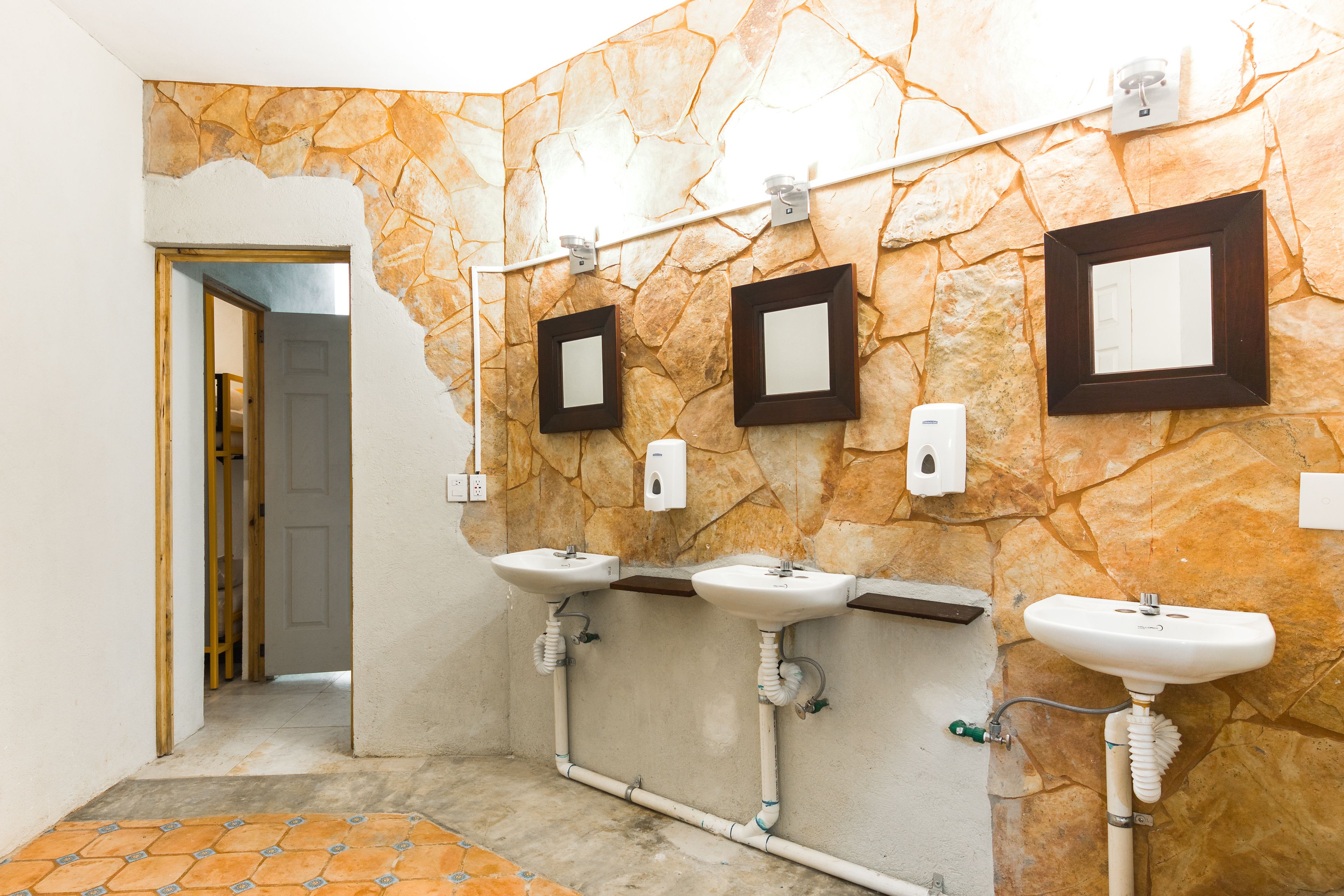 Une salle de bain avec trois lavabos, un mur en pierre et une porte donnant sur une autre pièce.