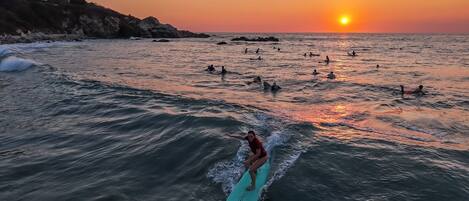 A sunset over a beach with people surfing and swimming.