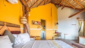 Une pièce comprenant un lit, une tête de lit en bois, un luminaire suspendu et une porte donnant sur une salle de bain.