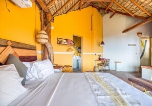 Een kamer met een bed, een houten hoofdbord, een hanglamp en een deur naar een badkamer.