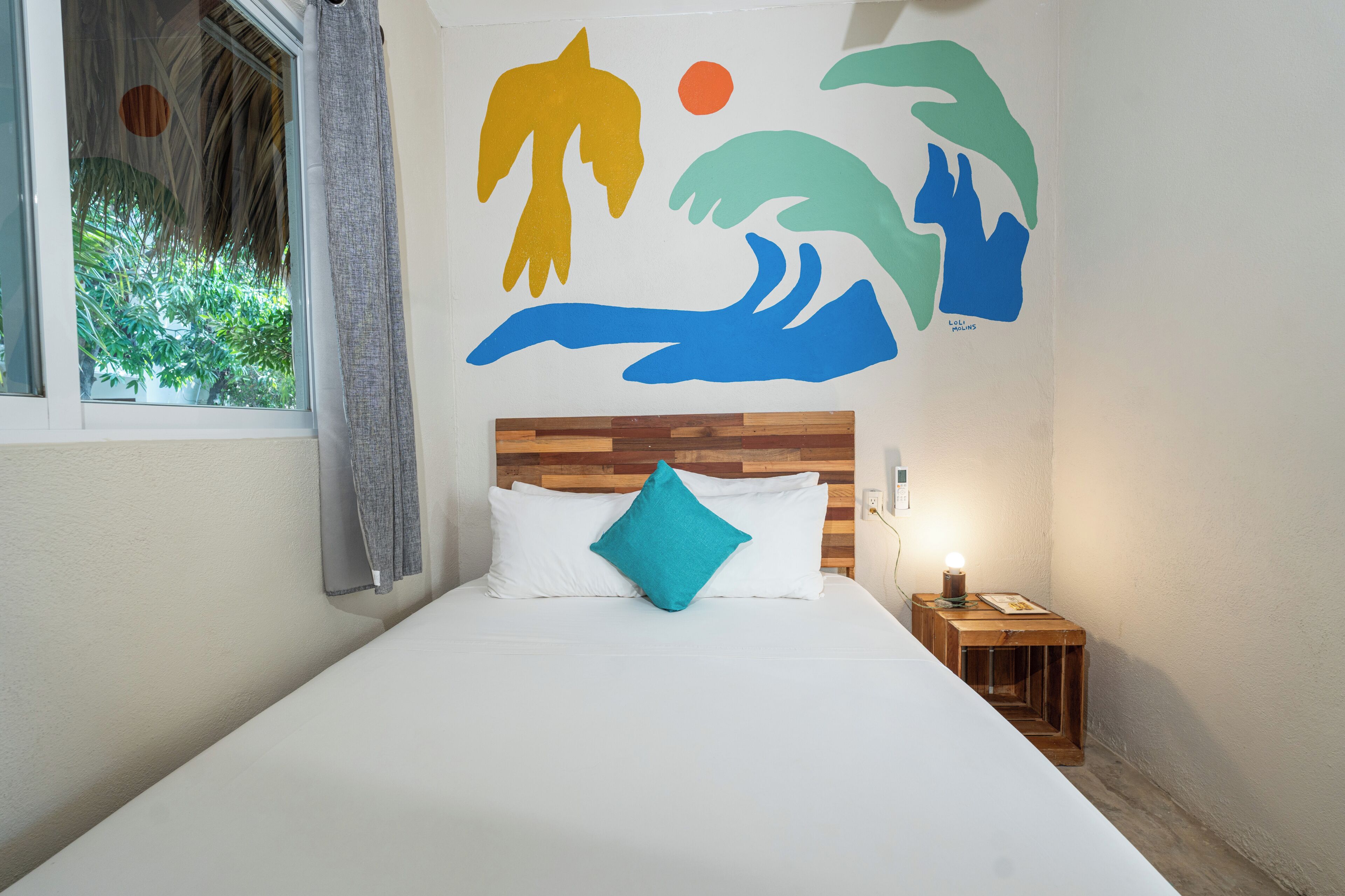 Une chambre à coucher avec une tête de lit en bois, une literie blanche, un coussin turquoise et une fresque murale.