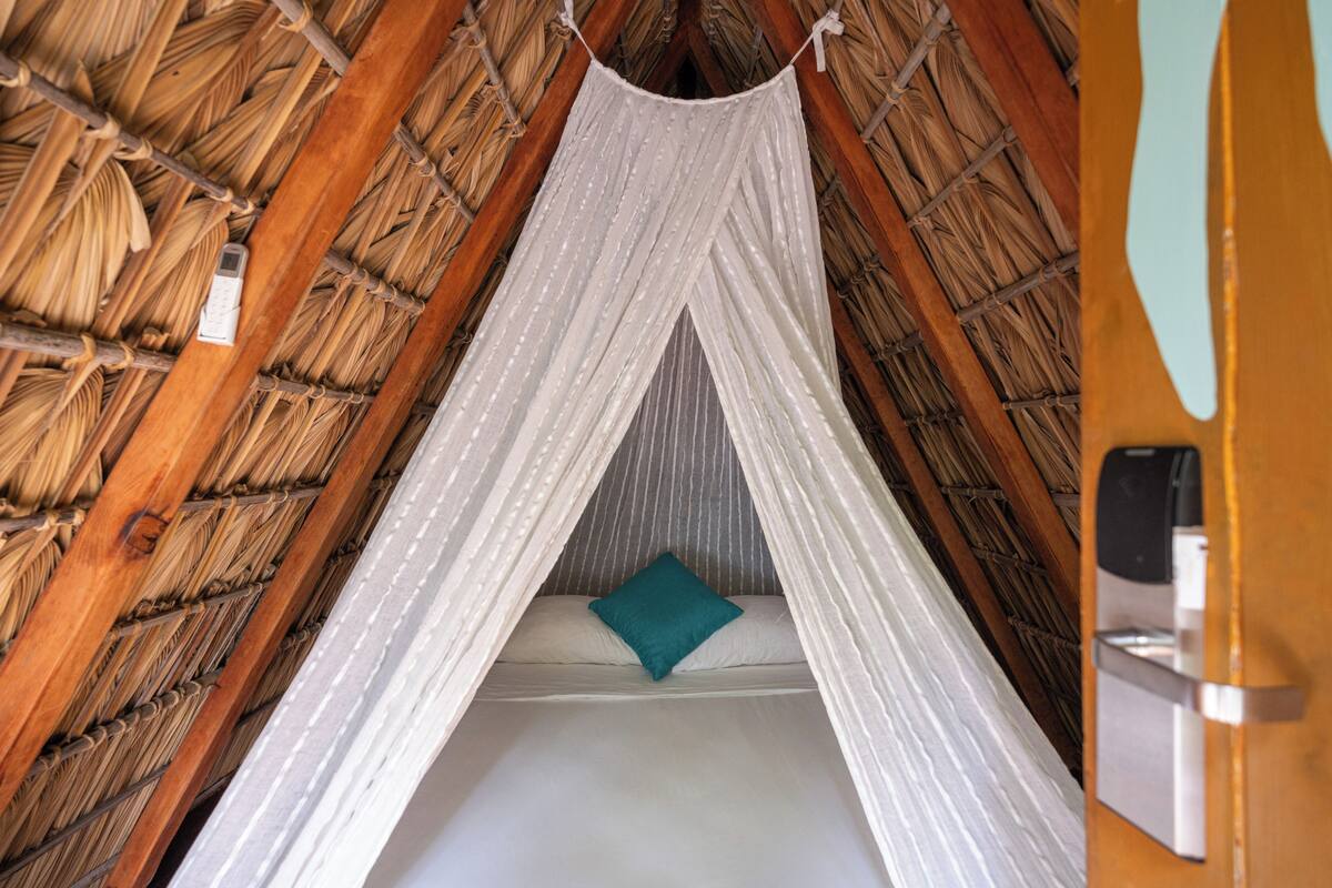 Una habitación con techo de paja y una cama bajo un dosel blanco.
