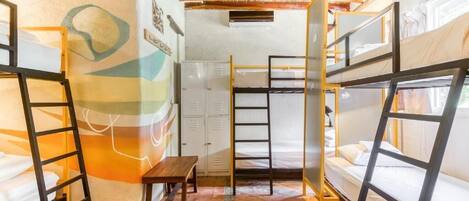 A dormitory room with bunk beds, a wooden ladder, a small table, and a wall with a geometric design.