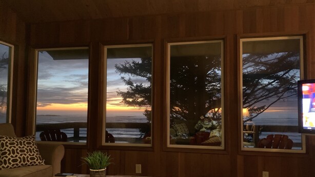 A living room with a large window overlooking a sunset, a wooden floor, and a sofa with patterned cushions.