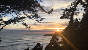 A sunset over a beach with waves, trees, and a rocky outcrop.