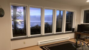 A room with a large window overlooking a body of water, a radiator below the windows, and a television on a stand to the right.