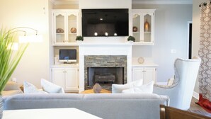 A living room with a fireplace, a television mounted above it, and a comfortable seating area with a sofa and armchairs. - Southern Luxury: Eastchase District 4bd / 3bth (Montgomery)
