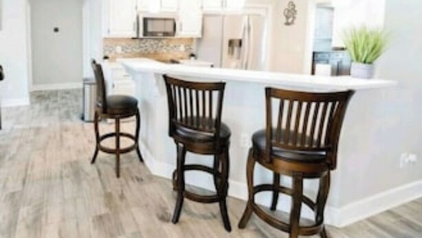 A modern kitchen with white cabinets, a central island with bar stools, pendant lighting, and a visible microwave. - Southern Luxury: Eastchase District 4bd / 3bth (Montgomery)