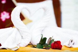 Un lit bien fait, agrémenté d’une serviette en forme de cœur et d’une rose rouge.