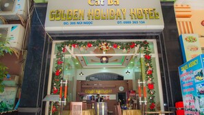 L’entrée de l’hôtel Golden Holiday, avec une enseigne au-dessus de la porte, un escalier menant à l’étage et une décoration de Noël visible à travers les portes vitrées.