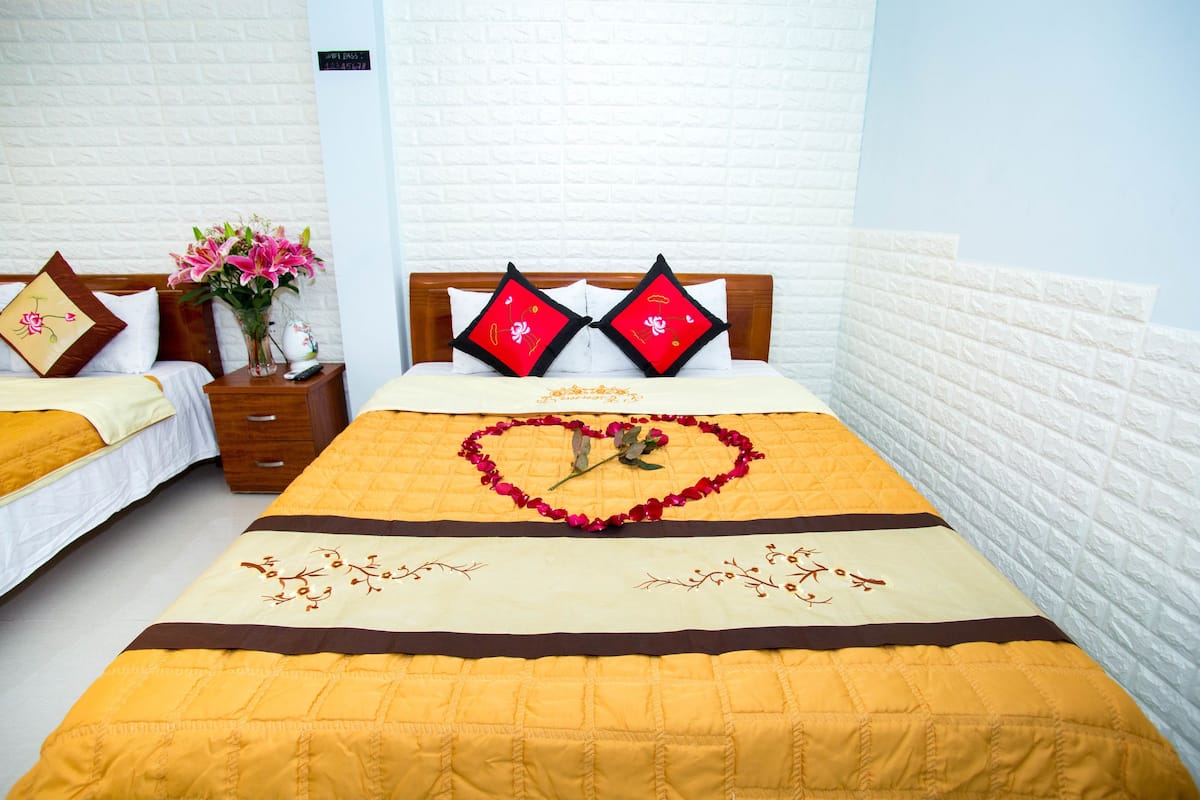A hotel room with two beds, a wooden headboard, a vase with flowers, and a heart-shaped decoration on the bed.