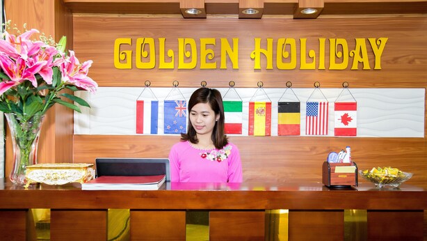Un comptoir d’accueil avec un revêtement en bois, une enseigne indiquant « GOLDEN HOLIDAY », et une rangée de drapeaux nationaux.