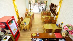 Un restaurant avec plusieurs tables et chaises, un réfrigérateur rempli de Coca-Cola et une bibliothèque contenant des livres et des objets décoratifs.