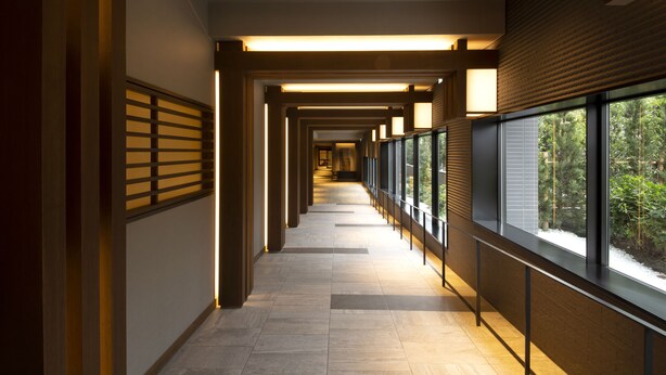 A corridor with a modern design, featuring a series of windows on one side and a wooden slat wall on the other.
