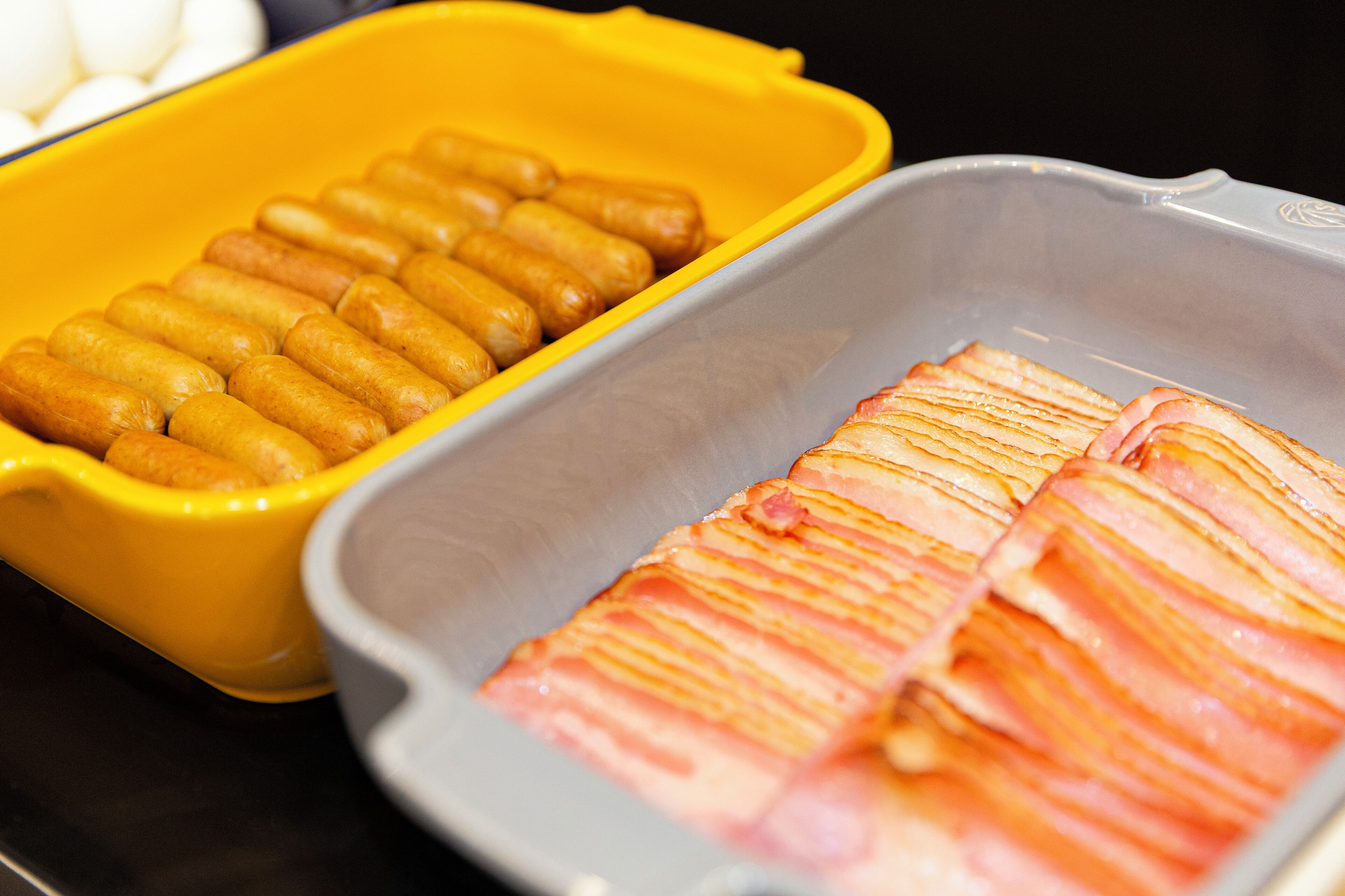A tray with sliced ham and a yellow container with fried items.