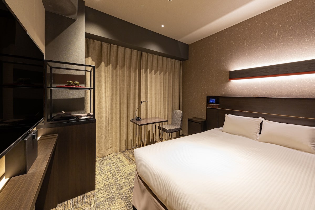 Ein Hotelzimmer mit Bett, Schreibtisch, Stuhl, Fernseher und einer Minibar.