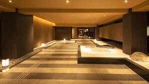 A hotel corridor with a checkered floor pattern, recessed lighting, and a reception area in the distance.