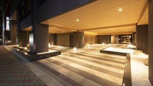 A modern hotel entrance with a spacious outdoor area, a reception desk, and a well-lit pathway.