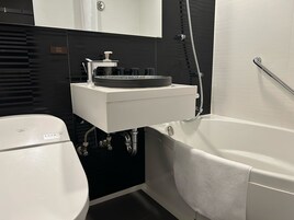 Un baño moderno con un lavamanos blanco, paredes revestidas de baldosas negras, un inodoro y una bañera.