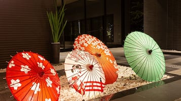 A row of traditional Japanese umbrellas in various colors, lined up on a pebbled surface in front of a building with a dark facade and glass windows.