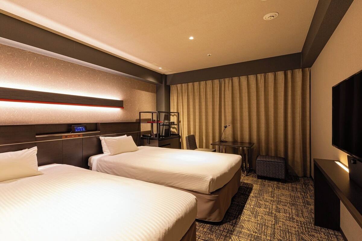 Ein Hotelzimmer mit zwei Betten, einem Schreibtisch, einem Fernseher und einer Minibar.