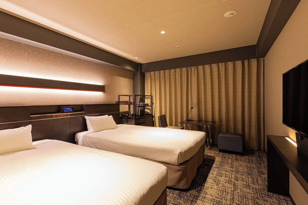 Ein Hotelzimmer mit zwei Betten, einem Schreibtisch, einem Fernseher und einer Minibar.