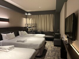 A hotel room with two beds, a desk, a TV, and a seating area.