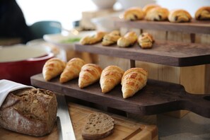 A wooden serving board with croissants and a loaf of bread on a wooden table.