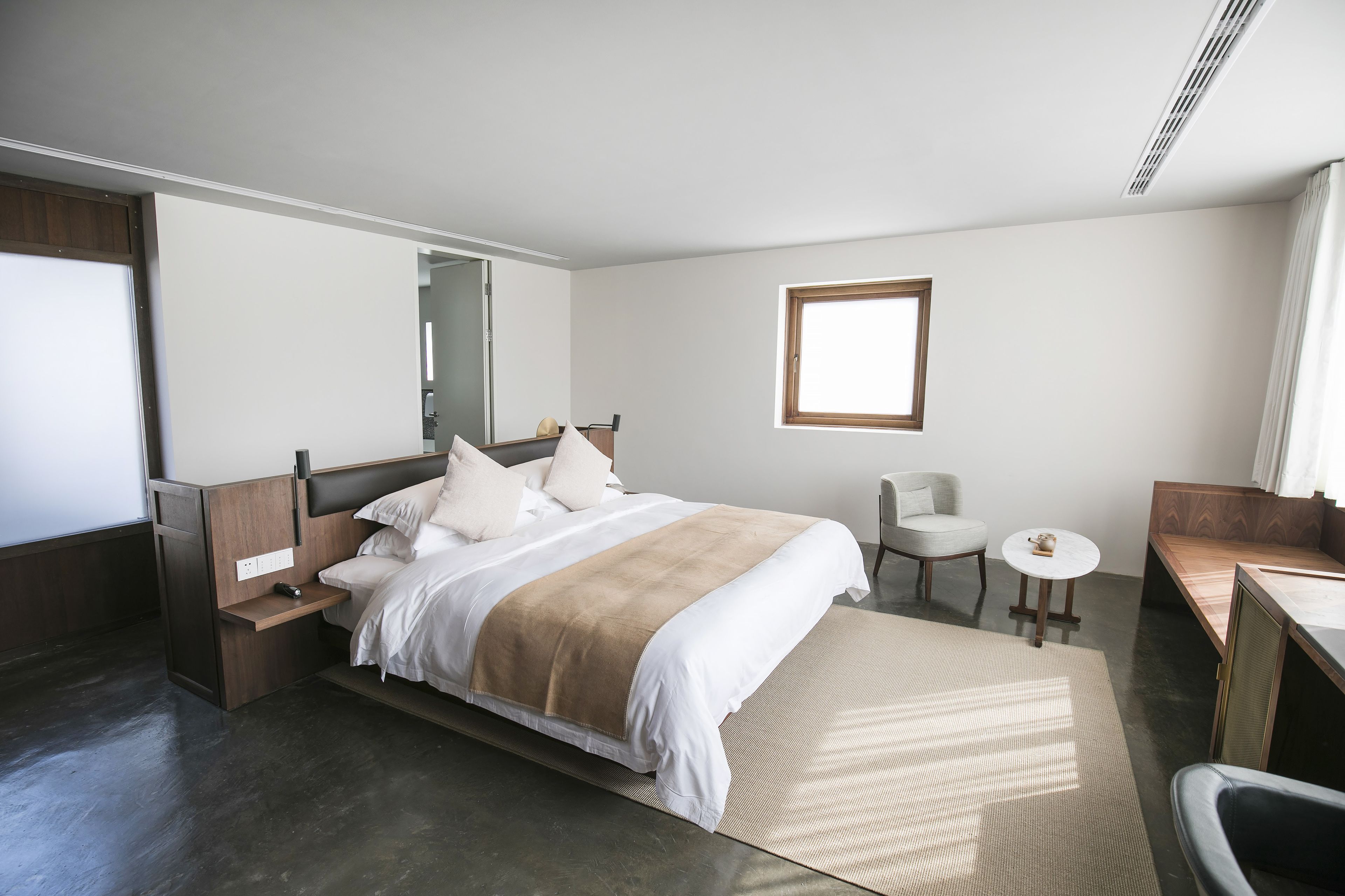 Una habitación de hotel moderna con una cama grande, un escritorio pequeño, una silla, una mesa redonda y un ventanal.