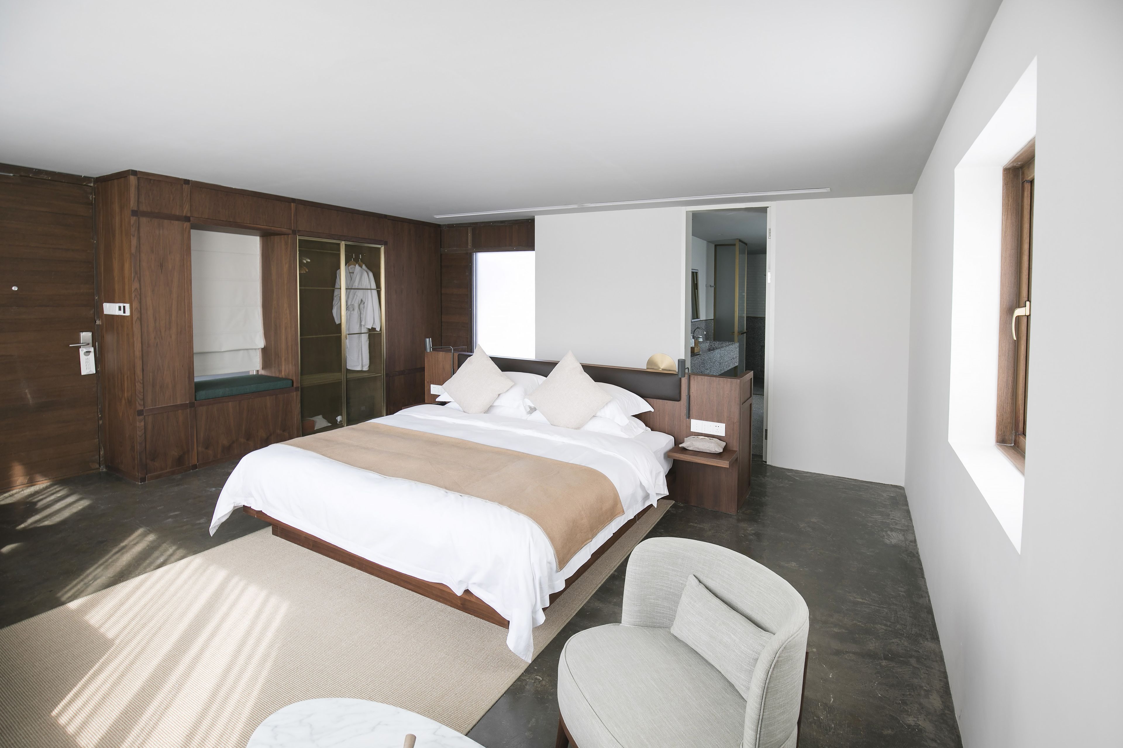 A modern bedroom with a large bed, a chair, a bedside table, a mirror, and a wardrobe.