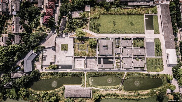 An aerial view of a modern building complex with multiple rectangular structures, a central courtyard, and surrounding green spaces.