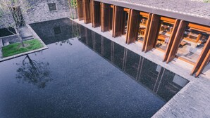 Un edificio moderno con una piscina reflectante, estructuras de listones de madera y un muro de piedra.