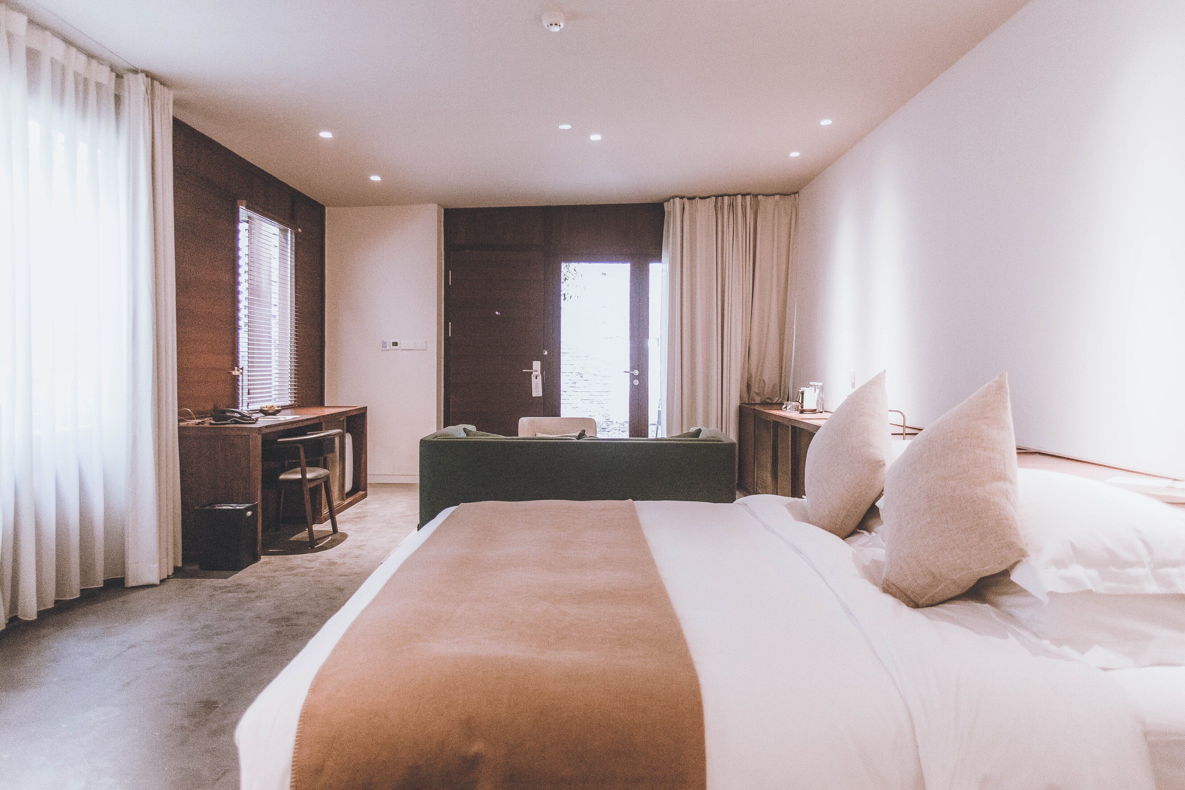 A hotel room with a large bed, a desk, and a chair. There is a window with curtains, and the room has a modern design.
